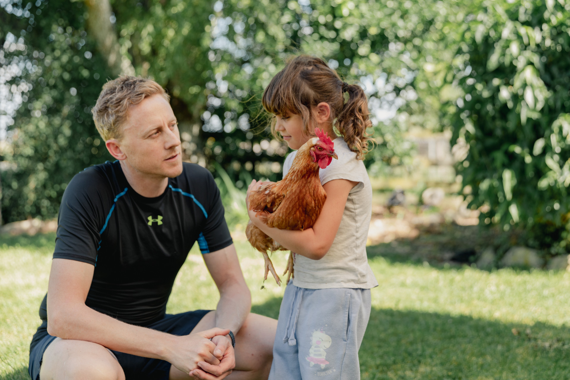 a man and a little girl holding a chicken in her arms